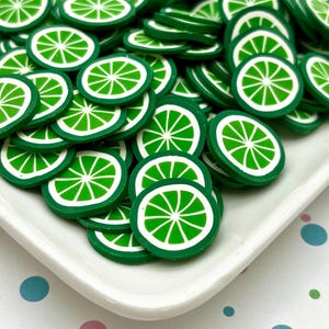 May include: A white plate filled with green and white lime slice shaped resin embellishments. The plate is on a background of colorful polka dots.