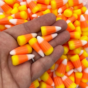 Op de afbeelding: Een close-up van snoepmaïs, een traditionele Halloween-lekkernij. De snoepjes zijn geel, oranje en wit, met een driehoekige vorm. Een hand houdt de snoepjes vast, met meer snoepmaïs op de achtergrond.