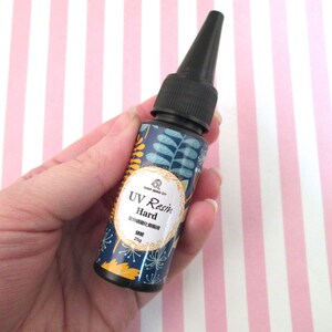 May include: A small bottle of UV resin with a black cap and a floral design label. The label reads "UV Resin Hard" and "25g".