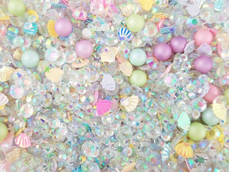 May include: A mix of iridescent clear, pink, and green glitter, seashells, and pearls.