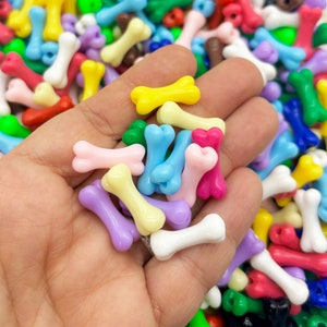 May include: A handful of colorful plastic bone-shaped beads. The beads are in various colors, including pink, blue, yellow, and purple.
