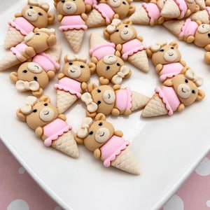 May include: A collection of brown teddy bear ice cream cone charms with pink bows and skirts. The charms are made of polymer clay and are perfect for adding a touch of whimsy to your crafts.