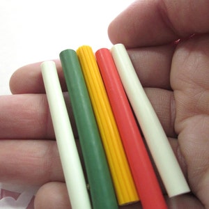 May include: Five colorful plastic dowels in white, green, yellow, red, and orange. The dowels are arranged in a row, with the white dowel on the left and the orange dowel on the right.
