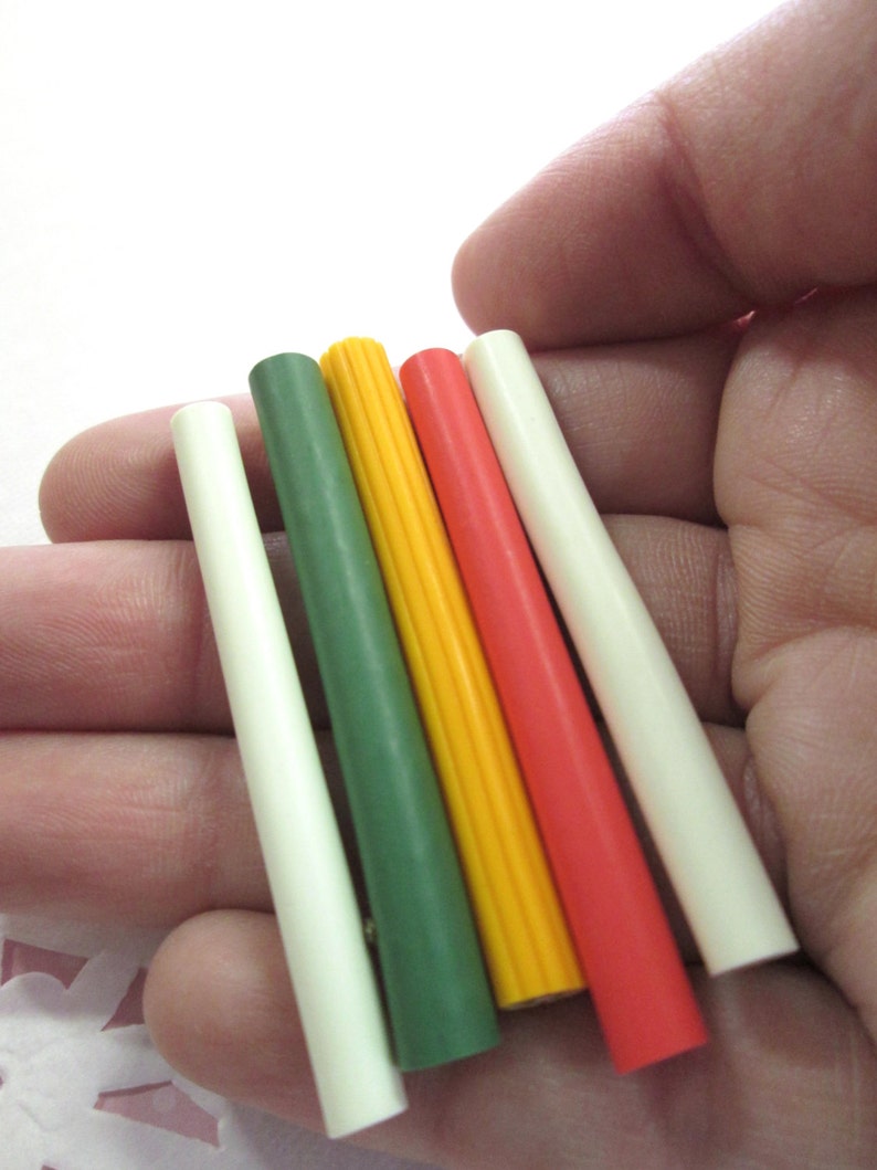 May include: Five colorful plastic dowels in white, green, yellow, red, and orange. The dowels are arranged in a row, with the white dowel on the left and the orange dowel on the right.