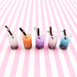 Pu&ograve; includere: Sei mini barattoli di vetro con cannucce nere e bubble tea colorato all'interno. I barattoli sono disposti in fila su uno sfondo a righe rosa e bianche.