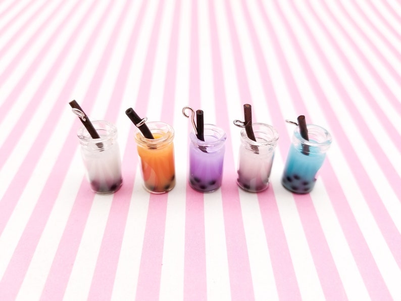 Pu&ograve; includere: Sei mini barattoli di vetro con cannucce nere e bubble tea colorato all'interno. I barattoli sono disposti in fila su uno sfondo a righe rosa e bianche.