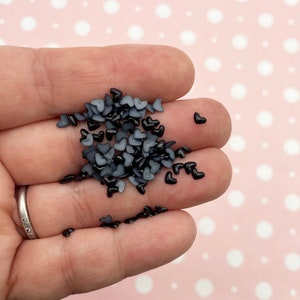 May include: A pile of small black and gray heart-shaped resin embellishments. These are great for adding a touch of sparkle to crafts and projects.