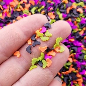 May include: A close-up of a hand holding a variety of small, colorful plastic bats. The bats are in shades of black, orange, green, and purple.
