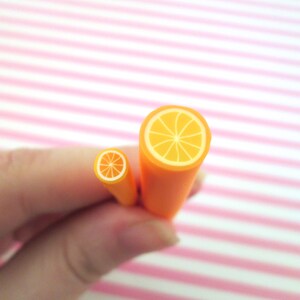 May include: Two orange polymer clay canes with a cross-section of an orange slice. The larger cane is about 1.5 inches in diameter and the smaller cane is about 0.5 inches in diameter.