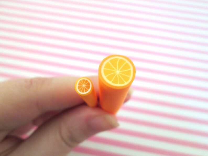 May include: Two orange polymer clay canes with a cross-section of an orange slice. The larger cane is about 1.5 inches in diameter and the smaller cane is about 0.5 inches in diameter.