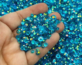 May include: A large pile of turquoise blue iridescent rhinestones. The rhinestones are various sizes and shapes.