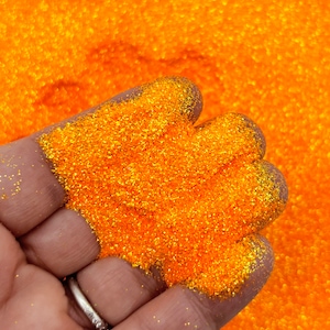 Peut inclure: Gros plan sur une main tenant une pile de paillettes orange vif. Les paillettes sont fines et brillantes, et elles reflètent magnifiquement la lumière.