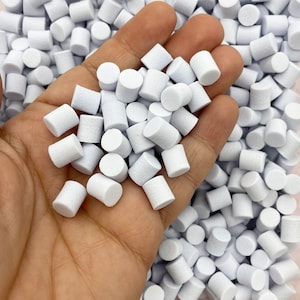 May include: A close-up shot displays a handful of small, white cylindrical objects. The objects are scattered across the image, with some held in a hand. The cylinders appear to be made of a porous material.