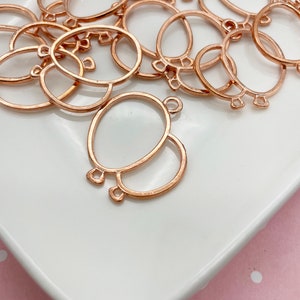 May include: A collection of rose gold-colored metal balloon-shaped charms. Each charm features an oval shape with a smaller circle attached below, and small loops for attaching to other objects. The charms are on a white surface.