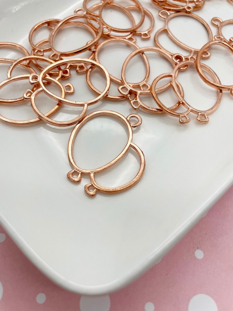 May include: A collection of rose gold-colored metal balloon-shaped charms. Each charm features an oval shape with a smaller circle attached below, and small loops for attaching to other objects. The charms are on a white surface.