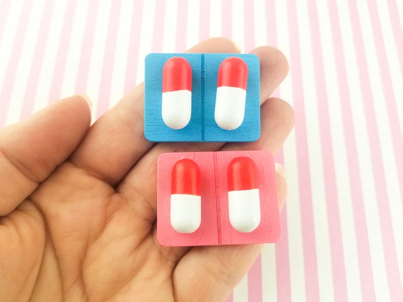 May include: Two sets of pill-shaped earrings, one set on a blue backing and one set on a pink backing. Each set has two earrings, each with a red top and a white bottom.