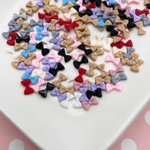 May include: A large assortment of colorful plastic bows in various colors, including pink, blue, red, black, white, and brown. The bows are scattered on a white plate.