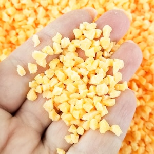 May include: A hand holding a small pile of bright orange and yellow dried fruit pieces.