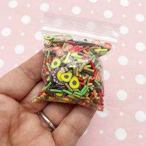 May include: A clear plastic bag filled with colorful polymer clay sprinkles. The sprinkles are shaped like avocado slices, red and yellow sticks, and brown and black sticks.