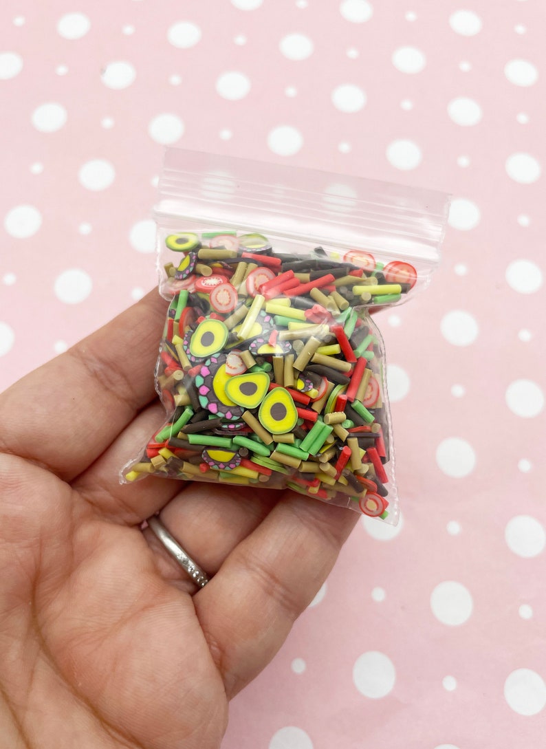 May include: A clear plastic bag filled with colorful polymer clay sprinkles. The sprinkles are shaped like avocado slices, red and yellow sticks, and brown and black sticks.