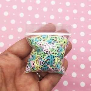 May include: A clear plastic bag filled with colorful heart-shaped sprinkles. The sprinkles are decorated with the words "OUIJA" and "ALINO" in black lettering.
