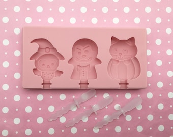 May include: Pink silicone mould with three Halloween-themed lolly shapes: an owl wearing a witch's hat, a vampire, and a cat wearing a pumpkin costume. Three clear plastic lolly sticks are included.