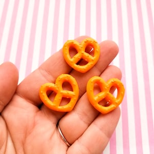 Può includere: Tre ciondoli a forma di cuore di pretzel arancioni. I pretzel sono in plastica e hanno una superficie testurizzata.