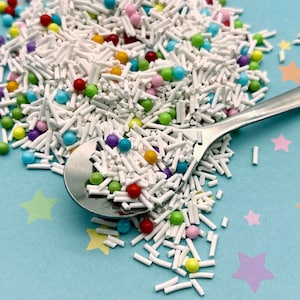 May include: A silver spoon filled with white sprinkles and colorful round sprinkles. The sprinkles are scattered on a blue background with white stars.