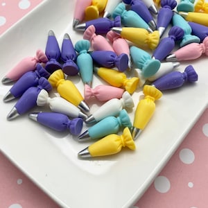 May include: A selection of small, colourful icing bags in pastel shades of pink, yellow, blue, purple, and white. Each bag has a silver tip. The bags are displayed on a white, rectangular plate.