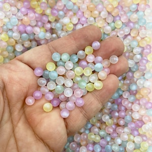 May include: A handful of small, iridescent, pastel-colored beads. The beads are a mix of soft yellow, pink, purple, and blue hues. The beads are round and smooth, and appear to be made of a shiny material.