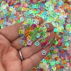 Peut inclure: Gros plan sur une poignée de paillettes en forme de patte d'animal de couleur arc-en-ciel irisé. Les paillettes sont de différentes couleurs, notamment rose, vert, bleu et orange.