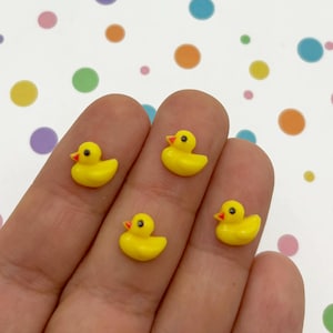 Può includere: Quattro piccole figure di anatre di gomma gialle con becchi arancioni e occhi neri. Le anatre sono disposte in fila sulla mano di una persona.