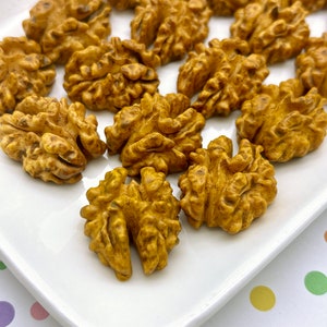 Könnte beinhalten: Nahaufnahme von geschälten Walnüssen, die ihre strukturierten, braunen Oberflächen zeigen. Die Nüsse sind auf einem weißen, rechteckigen Teller angeordnet und bieten einen detaillierten Blick auf ihre komplizierten Muster. Das Bild hebt die natürliche Farbe und Form der Walnüsse hervor.