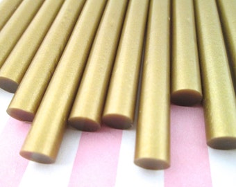 May include: A close-up of a group of gold wax sticks. The sticks are arranged in a fan shape and have a shiny, metallic finish.