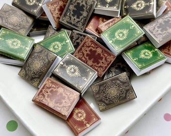 May include: A collection of miniature books in various colors, including green, red, and black, with gold embossed designs. The books are arranged on a white, rectangular plate, creating a visually appealing display.