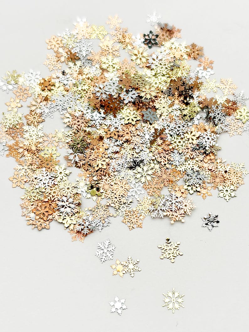 a collection of small, metallic snowflake-shaped pieces in various colors, including gold, silver, and white, scattered across a plain background.