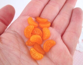 May include: A collection of small, orange, plastic, citrus fruit slices. The slices are arranged in a hand.