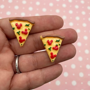 Puede incluir: Dos rebanadas de pizza amarillas con cabezas de Mickey Mouse rojas y coberturas verdes. Las rebanadas de pizza están hechas de arcilla polimérica.