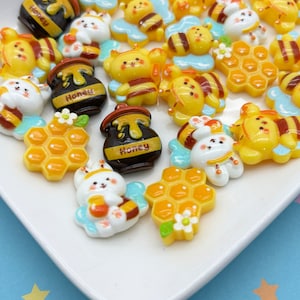 May include: Assortment of resin charms featuring bees, honey pots, honeycombs, and bunnies. The charms are yellow, brown, white, and blue. The charms are perfect for adding a touch of whimsy to crafts and jewelry.