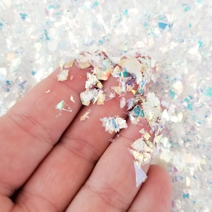 Könnte beinhalten: Nahaufnahme von irisierenden weißen Glitzerflocken, mit einer Hand, die eine kleine Menge Glitzer hält. Der Glitzer ist perfekt, um Bastelarbeiten, Harzprojekten und vielem mehr Glanz zu verleihen.