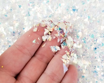 Könnte beinhalten: Nahaufnahme von irisierenden weißen Glitzerflocken, mit einer Hand, die eine kleine Menge Glitzer hält. Der Glitzer ist perfekt, um Bastelarbeiten, Harzprojekten und vielem mehr Glanz zu verleihen.
