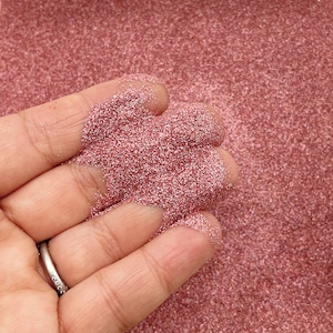 May include: A close-up of a hand holding a pile of rose gold glitter. The glitter is fine and shimmery, and it catches the light beautifully.
