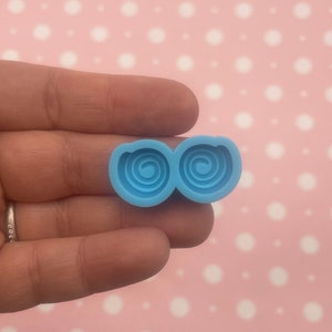 Puede incluir: Un molde de silicona azul claro con dos cavidades circulares, cada una con un diseño en espiral.