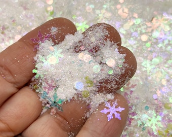 Op de afbeelding: Een close-up van iriserende witte glitter met sneeuwvlok- en cirkelvormen. De glitter zit in een hand, klaar om te worden gebruikt voor knutselen.