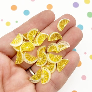 Può includere: Una collezione di piccoli ciondoli a forma di fetta di limone giallo traslucido realizzati in resina. Ogni pezzo presenta un motivo dettagliato a spicchi di agrumi con una buccia esterna trasparente e un interno giallo vivace, ideati come decorazioni.