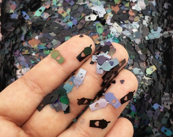 Pode incluir: Uma mão segurando glitter preto e verde iridescente em forma de xícaras com corações. O glitter está espalhado em uma superfície preta.
