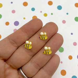 May include: Three small yellow and black bee figurines with white wings. The bees are on a hand.