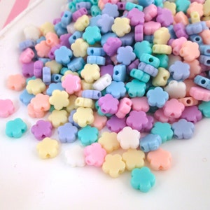 Puede incluir: Un mont&oacute;n grande de cuentas de pl&aacute;stico con forma de flor de color pastel. Las cuentas son en tonos de rosa, azul, amarillo y morado.