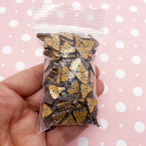 May include: A clear plastic bag filled with small brown and yellow resin poop emoji charms. The charms have a cute cartoon face with two eyes.