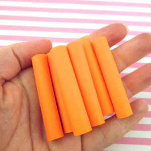 May include: Six orange polymer clay tubes, approximately 1.5 inches long, are held in a hand. The tubes are smooth and have a matte finish.
